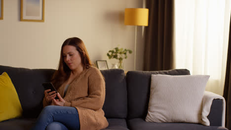 Mujer-Sentada-En-Un-Sofá-En-Casa-Viendo-Una-Película-O-Programa-O-Navegando-Por-Internet-En-Un-Teléfono-Móvil-2